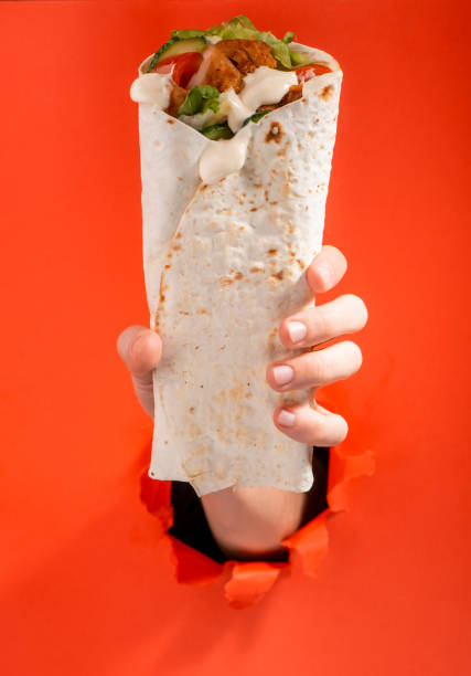 istock Hand giving a doner roll through a torn hole in red paper background 1301180469