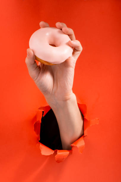 istock Hand showing a pink doughnut through a torn hole 1301180667