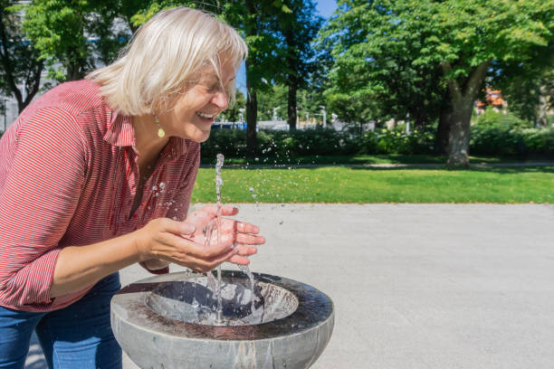 Mature woman refreshes from a drinking water fountain in summer stock photo