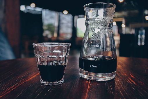 Half cup of v60 black coffee and unique beaker coffee glass jar on the wooden table.