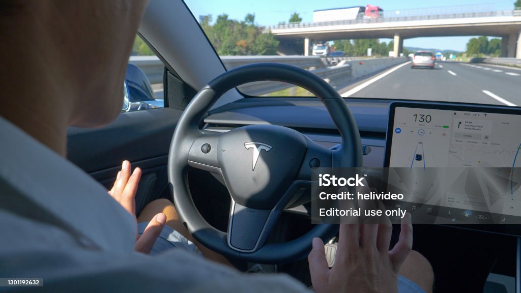 CLOSE UP Unrecognizable man tentatively lets go of the steering wheel of a Tesla TESLA CAR, SLOVENIA, APRIL 2020: CLOSE UP: Unrecognizable man tentatively lets go of steering wheel of a Tesla after setting autonomous vehicle on auto-pilot. Man gives control to self-steering car Driverless Car Stock Photo