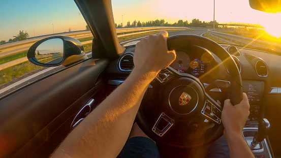 HIGHWAY IN SLOVENIA, AUGUST 2020: POV, LENS FLARE: First person shot of cruising down freeway in a Porsche at golden sunset. Driving a brand new sportscar down an empty highway crossing rural Slovenia