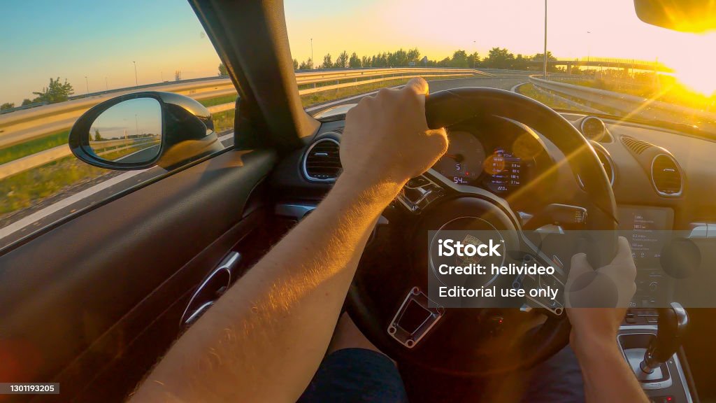 POV: First person shot of cruising down the freeway in a Porsche at sunset. HIGHWAY IN SLOVENIA, AUGUST 2020: POV, LENS FLARE: First person shot of cruising down freeway in a Porsche at golden sunset. Driving a brand new sportscar down an empty highway crossing rural Slovenia Porsche Stock Photo