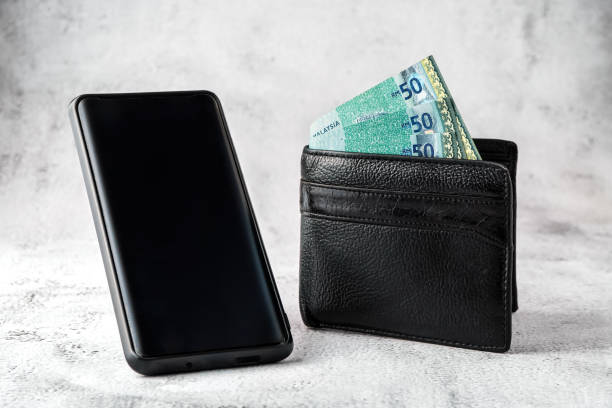 istock Ringgit Malaysia notes in the black wallet and black mobile smartphone on grunge white backdrop 1301194192