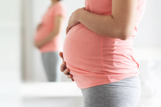 close-up pregnant woman in pink shirt standing touching her belly with copy space. - new childbirth new life love imagens e fotografias de stock