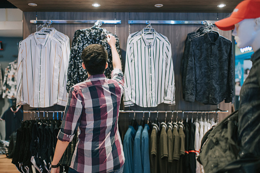 Asian chinese male hand holding menswear shirt at clothing store choosing the right one shopping