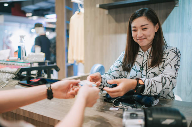 asian chinese boutique shop owner receiving credit card from her customer at cashier check out in menswear clothing store - clothing store paying cashier credit card imagens e fotografias de stock