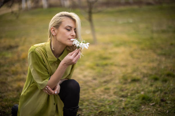 Young woman crouching in back yard on grass field and smelling snowflake flower