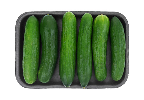 Top view of six small bite size dipping cucumbers in a row on a black foam tray isolated on white background.
