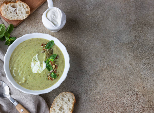 istock Broccoli cream soup served with mint, cream, seeds and fresh bread on concrete background. Healthy vegetarian food concept. Top view. 1301198467