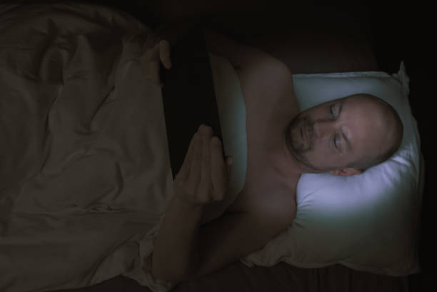 istock Man lying in bed at night looking at his tablet with harmful blue light illuminating his face. 1301199736