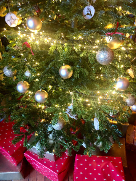 istock Image of wrapped presents beneath Christmas tree with bauble decorations and illuminated fairy string lights 1301200254