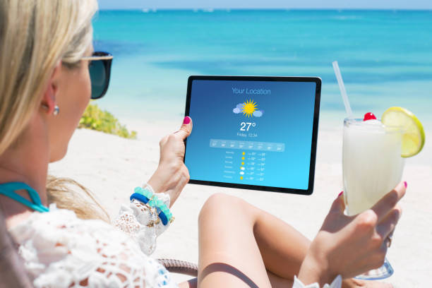 istock Woman viewing weather forecast on tablet while relaxing on the beach 1301200324