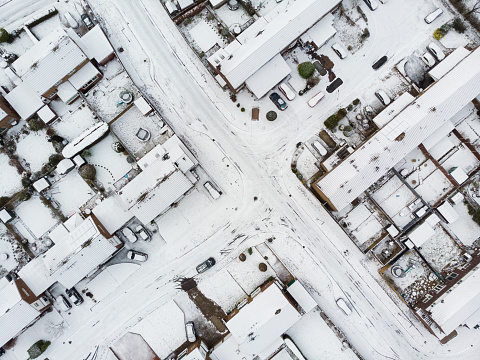 A winter view from directly above a series of streets with semi detached houses and gardens in southeast England, UK. The rooftops and streets are covered with a blanket of snow.