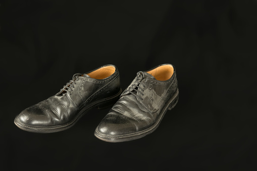 Old black men dusty leather shoes isolated on black background, unemployment concept