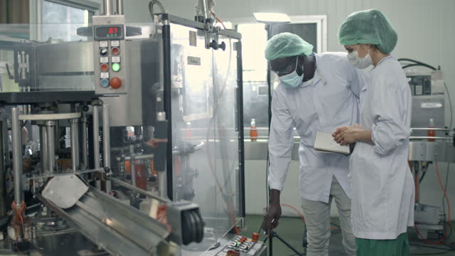 保護作業服の2つの多様な工場労働者は、コンベアベルト上の製品の品質を制御します