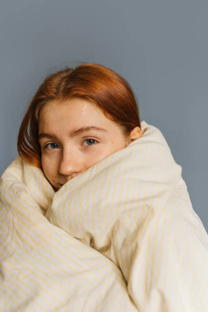 Close up portrait of woman wrapped in pastel blanket isolated over grey studio background. Ginger girl looking calmly at camera, feeling happy, enjoying morning time
