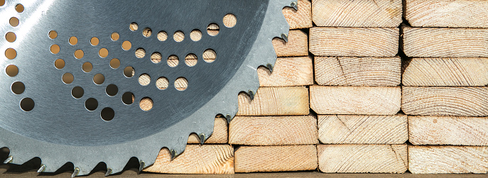 Detail of circular saw metal blade placed wooden planks in carpentry workshop