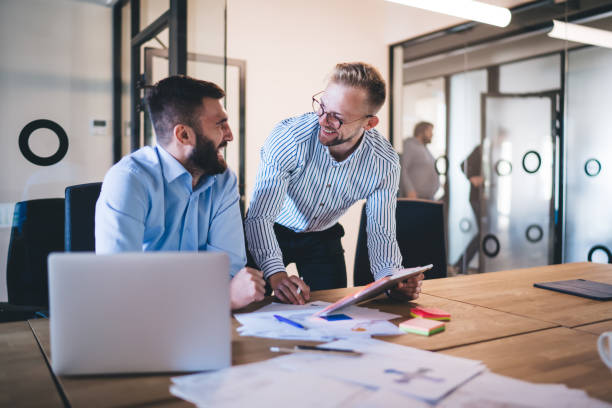 istock Happy male colleagues enjoying friendly briefing during working time at table desktop using modern technology for browsing web publications, Caucasian professionals discussing project and smiling 1301209868