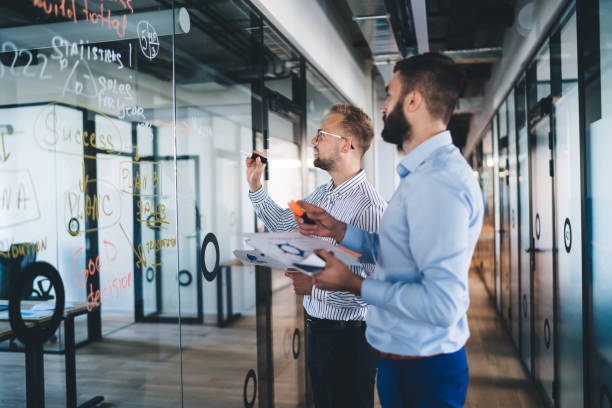 istock Confident man spending time for training business person writing information on modern board during cooperation with partner discussing ideas for startup project, accounting briefing in office 1301209931