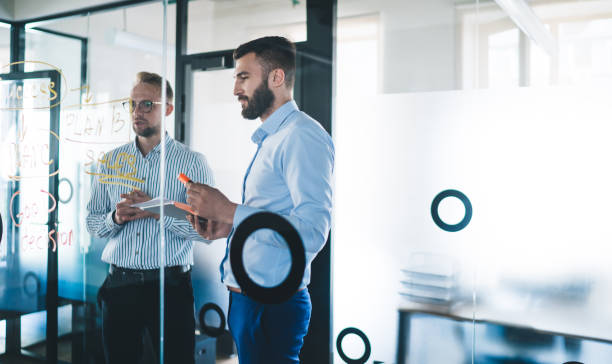 istock Smart casual Caucasian male employees discussing business information while cooperating and creating idea for startup project near modern glass board in office interior, entrepreneurship concept 1301209943