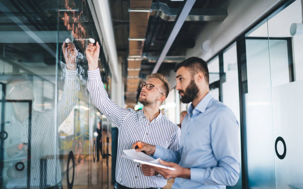 istock Confident male employees cooperating on working process in business workspace, Caucasian men colleagues talking while planning and analyzing analytic from glass board during brainstorming meeting 1301209950