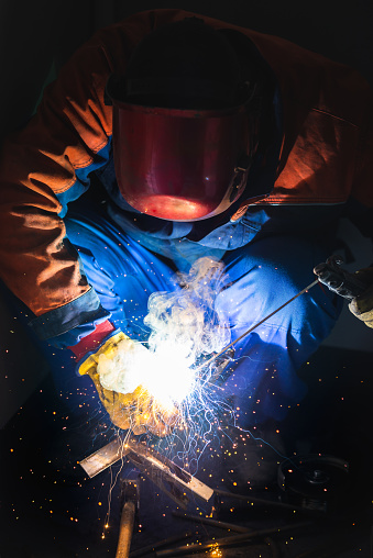 Welding concept. Industrial worker or welder wears protective mask and gloves erects technical steel on factory. Labour worker welds metal. Man repairs detail in cars auto service. Steel worker