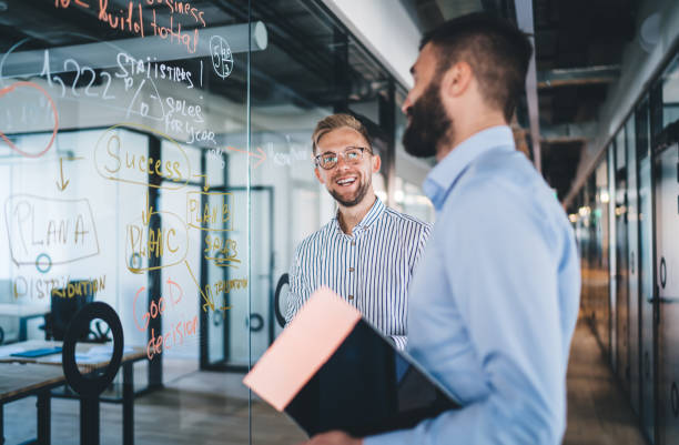 istock Happy male colleagues enjoying friendship on work smiling while discussing project ideas, cheerful businessmen brainstorming on financial analytic standing in workspace with glass board and laughing 1301209958
