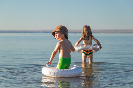 Boy and girl with rubber rings resolutely go to sea to learn to swim.