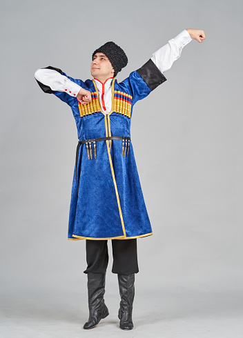 A young Caucasian man is dressed in a Georgian traditional clothing and a male headdress. The male dancer is showing a poses of folk dance. He is looking at the camera. Studio shooting