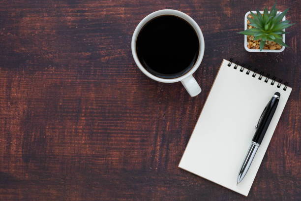 istock Top view of open school notebook with blank pages, coffee cup and pen for taking write notes on wood table background. Flat lay, creative workspace office. Business-education concept with copy space. 1301212238