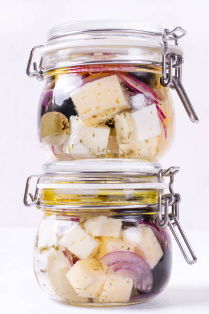 Tasty feta cheese with oil's drop on fork at glass jar. Cheesse with tomatoes and spices on marble background