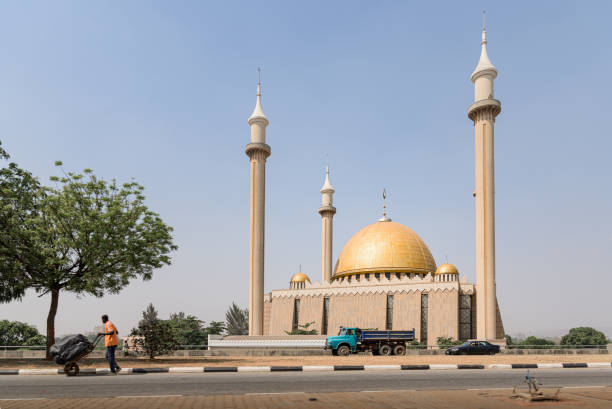 National Mosque landmark, Abuja, Nigeria Abuja, Nigeria - 27 Jan 2021: A man pushes a cartwheel along an empty highway in front of the National Mosque landmark building in Abuja, Nigeria. The West Africa city sees no street traffic following Covid-19 confinement restrictions. abuja stock pictures, royalty-free photos & images