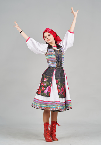 A young caucasian woman with dark hair is dressed in a Moldavian traditional clothing. The young female dancer is dancing national dance and showing traditional poses. She is smiling looking at the camera. Studio shooting