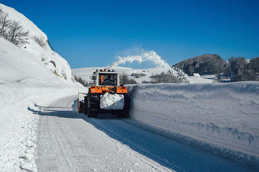 A snowplow truck removing snow from a winding rural road on bright winter day.