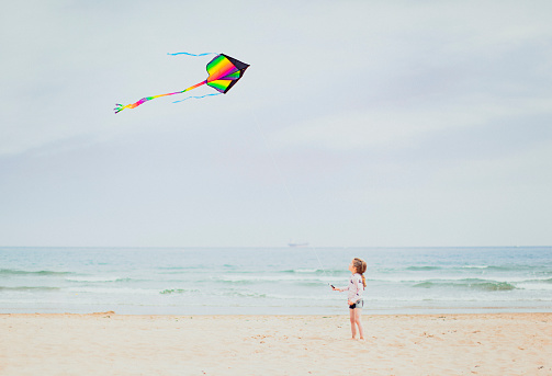A little girl is alone on a beach flying a kite for the first time