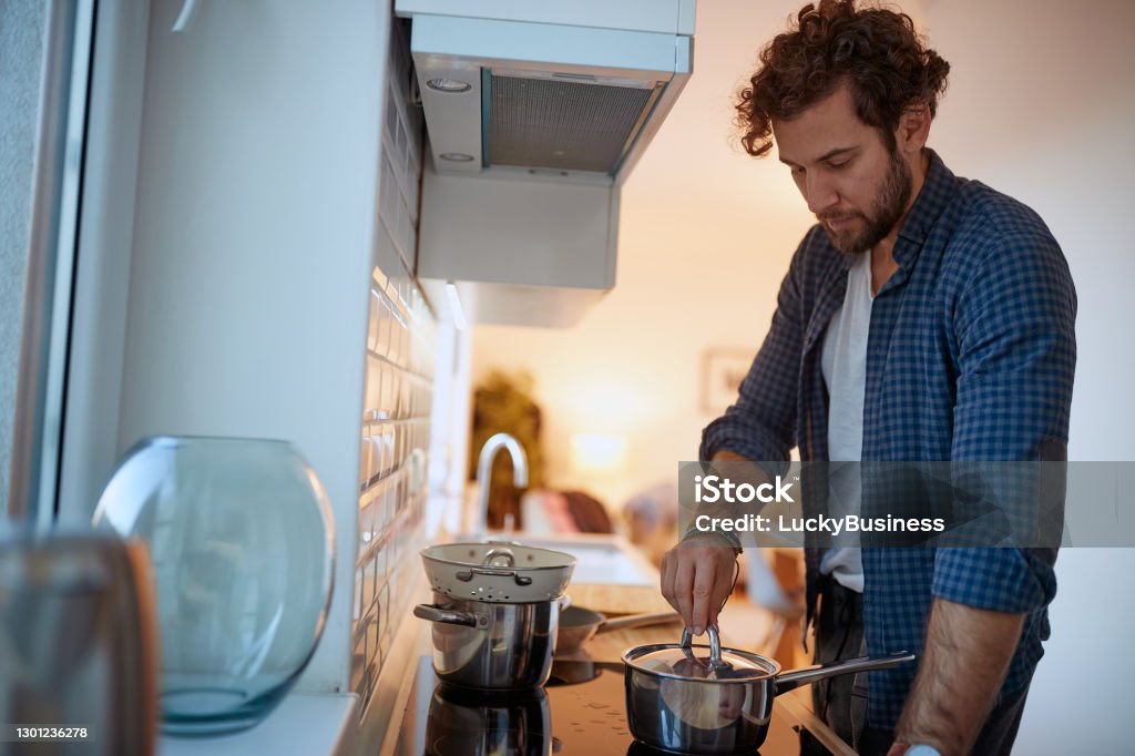 Young man preparing a meal on a stove in the kitchen. Kitchen, housework, quarantin, home Young man preparing a meal on a stove in a relaxed atmosphere in the kitchen. Kitchen, housework, quarantin, home Boredom Stock Photo