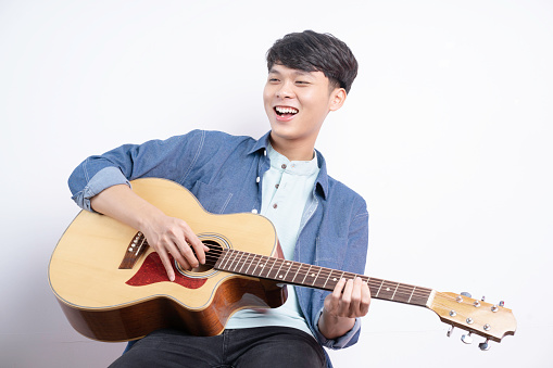 Young man playing guitar and singing on white background