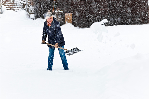 Smiling woman with nordic knit hat shoveling snow during heavy snowfall.