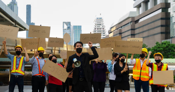 Group of young people wearing face mask and activists protesting in the city Group of people in different career wearing protective face mask protesting and raising banners in the city for justice and equal rights . A man in black suit with raising hand and holding megaphone, demonstration concept. labor union stock pictures, royalty-free photos & images