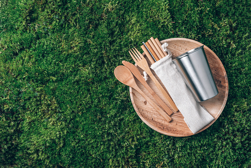Sustainable lifestyle. Zero waste, plastic free, recycling concept. Stainless steel cup, wooden spoon, fork, knife, lunch plate and drinking bamboo straw on green grass, moss background.