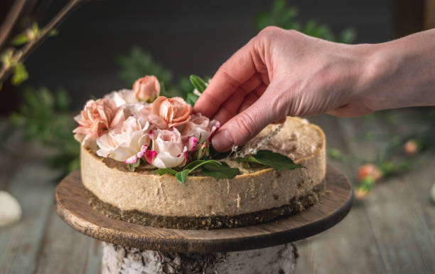 istock Decorator's hand is decorating the delicious raw mousse cake with tenderness pink flowers. Concept of romantic mood and spring atmosphere 1301239040