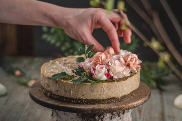 istock Decorator's hand is decorating the delicious raw mousse cake with tenderness pink flowers. Concept of romantic mood and spring atmosphere 1301239045