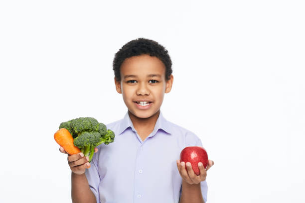афроамериканский мальчик держит в руках овощи и фрукты. концепция здоровой вегетарианской пищи для детей - apple healthy eating eating black стоковые фото и изображения