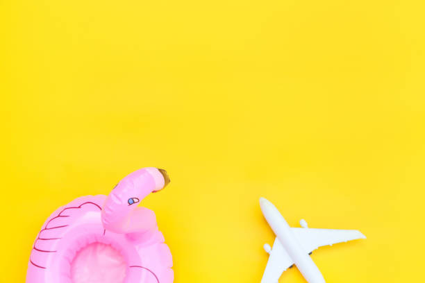 istock Summer beach composition. Minimal simple flat lay with plane and Inflatable flamingo isolated on yellow background. Vacation travel adventure trip concept. Top view copy space 1301241294