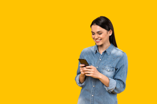 istock Chatting online. Caucasian satisfied girl texting online using her smartphone, typing message to friends or boyfriend, standing against isolated orange background and smiles 1301241768