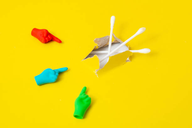 istock Cotton stick for cleaning the ear on a yellow background. Multi-colored hands point to her. 1301244181