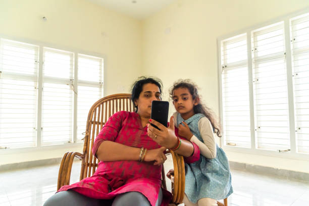mutter und tochter beobachten handy zu hause - mobile phone photography bangalore offspring stock-fotos und bilder