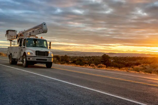 Photo of A Bucket Or Aerial Platform, Boom Truck Driving Through The Desert Of Utah, Near Moab, Wilson Arch, With A Dramatic Sunset To The West