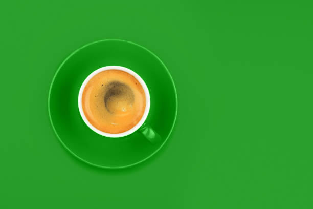 One full espresso coffee cup with saucer over vivid green paper background, elevated top view, directly above